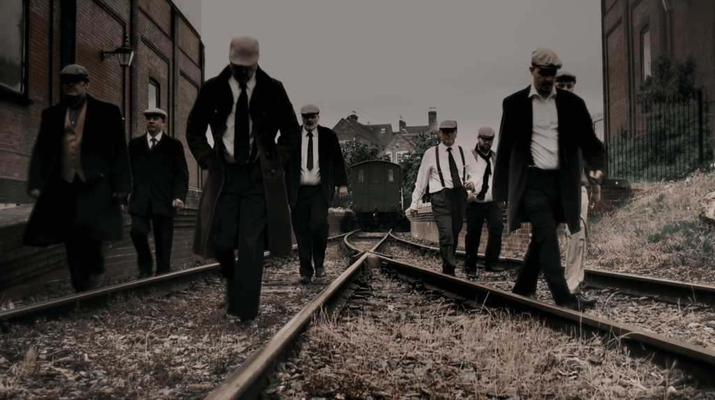 Men in shirts and ties walk the tracks at a murder mystery event